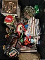 View of various miscellaneous decorative items including Coca-Cola tins, animal figurines, and boxed items stacked densely.