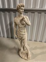 Front view of large male figurine sculpture posed standing with one hand on chest