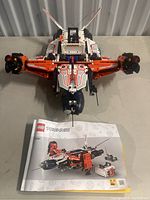 Top down view showing the Lego Technic cargo helicopter with extended rotors and cockpit, positioned above the instruction manual featuring set 42181 cover.