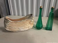 Photo showing the marked beige ceramic planter with horizontal ridges alongside two green glass bottles with corks.