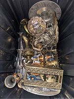 Photo of metal lot in bin showing various metal items including embossed plates, vases, figurines and stands