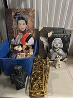 Wide shot of the lot showing framed prints, decorative wall piece, figurines, and blue bin with miscellaneous items.