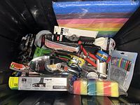 Photo showing mixed lot of kitchen and hand tools, craft markers, and cleaning sponges in a black container.