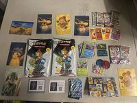 Photo of various sealed and unsealed Pokémon cards and booster packs laid out including promotional items and trading tokens.