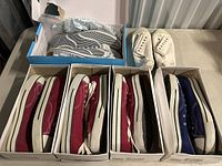 Four pairs of casual sneakers displayed in boxes and on surface, including red, navy blue, white, and striped designs.