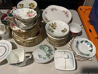 Photo showing multiple stacks of teacups, saucers, and serving bowls with varied floral patterns and gold accents.