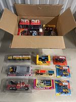 Wide shot of all toy cars and trucks in box and arranged on surface, showing variety and packaging