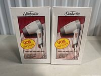 Photo of two boxed vintage Sunbeam hair dryers, model 1500 Dust Turbo, with VO5 free sample stickers on the boxes.