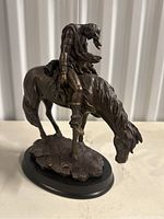 Left angle view of the bronze sculpture showing detailed warrior on horse with horse grazing and warrior slumped forward.