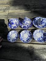 Photo shows three tea cups and three saucers arranged on wooden table featuring detailed blue and white oriental Mikado pattern