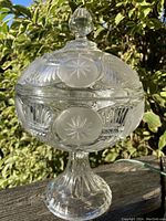 Full view of the covered compote showing the lid with star etched circular motifs and the pedestal base with fluted detail under natural light.