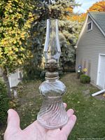 Full view of the miniature oil lamp held outdoors showing its shape, glass clarity, and metal burner.