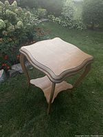 Photo showing full square scalloped oak parlour table with curved legs on a grassy outdoor background.