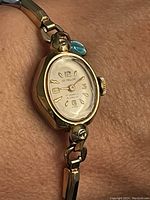 Front view of the ladies Ed. Heller watch showing gold-tone oval case, white dial, gold-tone numerals and indices, and stretch band.