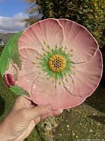 Side view showing the flower-shaped ceramic plate held outdoors with pink petals, green stems, and yellow center.