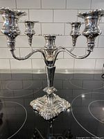 Five arm silver plated candelabra on a black stove top, showing its polished surface and intricate design details.
