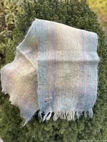 Full view of the multi-color pastel mohair scarf draped over greenery, showing colors and texture.