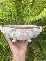 Full view of the footed oval porcelain planter with hand painted floral design and reddish-brown rim.