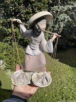 Full view of the LLadro figurine being held outdoors showing balance baskets with fish and traditional attire.
