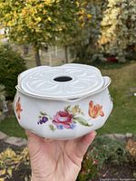Porcelain bowl with floral design and fitted lid with hole in center shown outdoors handheld