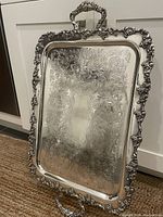 Full front view of the large silver serving tray standing vertically showing ornate grapevine border and handle detail.