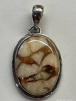 Front view of the oval pendant showing beige and brown patterned stone set in wide sterling silver bezel.