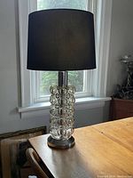 Front view of lamp on wooden table with black shade and glass bubble column