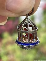 Close-up side view of sterling silver birdcage pendant with red bird inside and blue enamel decoration on base