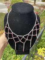 Front view of garnet lavaliere necklace displayed on black bust showing symmetrical geometric pattern of garnet beads and chain.