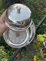 Three piece domed muffiniere with intricate engraving held outdoors showing the top and inner part separated