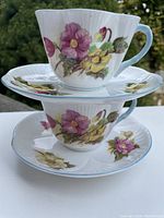 Two Shelley porcelain cups and saucers stacked, showing floral pattern and light blue rim detail.