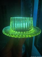 Vaseline uranium glass bowl with attached plate glowing bright green under UV light, showing ribbed texture and patterned plate edge.