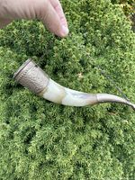 Side view of vintage powder horn showing elongated curved horn body with embossed metal cap at wider end.