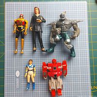 Top view of five action figures including yellow and black robot, female character in black suit, grey spiked monster, small male figure, and red robot transformer.