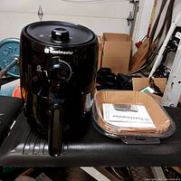 Toastmaster black air fryer with front control dial and handle shown on black surface in garage setting.