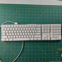 Full view of the white Apple wired keyboard showing all keys including numeric keypad, resting on a green cutting mat.