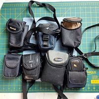 Photo showing seven different black fabric camera bags and pouches of various brands and styles on a green cutting mat.