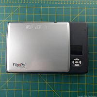 Top view of closed FlipPal mobile scanner showing silver lid with logo and black control section with screen and buttons