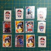 Grid layout of hockey stickers and trading cards on a green cutting mat. Showing goalie mask sticker decals and multiple hockey player trading cards.