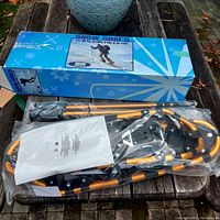 Snowshoes and walking poles partially wrapped in plastic placed on wooden surface