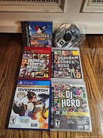 Photo showing six Playstation video games including PS1, PS3, and PS4 titles arranged on a wooden floor with visible cover art and cases.