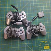 Four Sony PlayStation 1 wired controllers arranged with cables wrapped, showing front face with buttons and analog sticks.