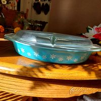 Side view of blue Pyrex divided casserole with white snowflake pattern and clear divided glass lid on a wooden table