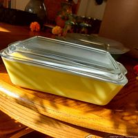 Yellow Pyrex rectangular glass casserole dish with clear glass lid, shown from the side on a wooden table.