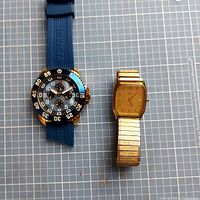 Two watches lying side by side, Invicta on left with blue strap and Timex on right with gold strap.