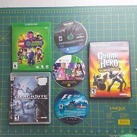 Photo showing 6 game discs including LEGO DC Super-Villains Xbox One in case, Guitar Hero World Tour PS2 in case, BlackSite Area 51 Xbox One in case, and loose discs for Call of Duty PS4, The Secret Saturdays Xbox 360, F1 2012 PS3.