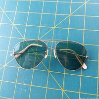 Front view of vintage aviator glasses showing gold filled frame and green lenses on blue grid mat.