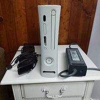Front view of the white Xbox 360 console standing upright with power button, disc drive and sensor window visible, along with power adapter and Kinect sensor.