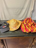 Photo showing the Molson Canadian visor, natural straw hat with ribbon, and colorful striped bag together on black surface.