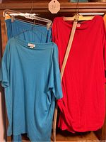 Light blue short sleeve top and pants alongside red long sleeve top with beige/gold belt and skirt hanging on rack.